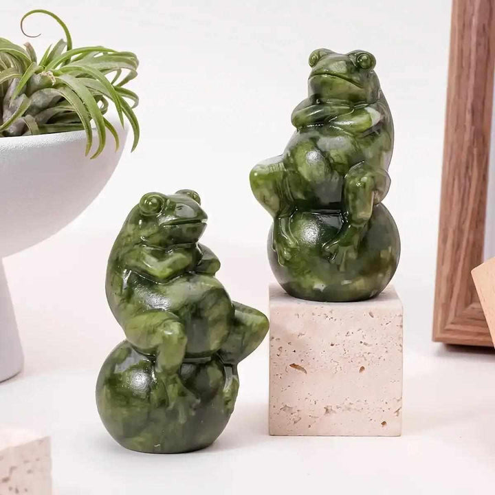 Two polished Serpentine Jade frog carvings seated on round balls, featuring mottled forest and olive green tones.