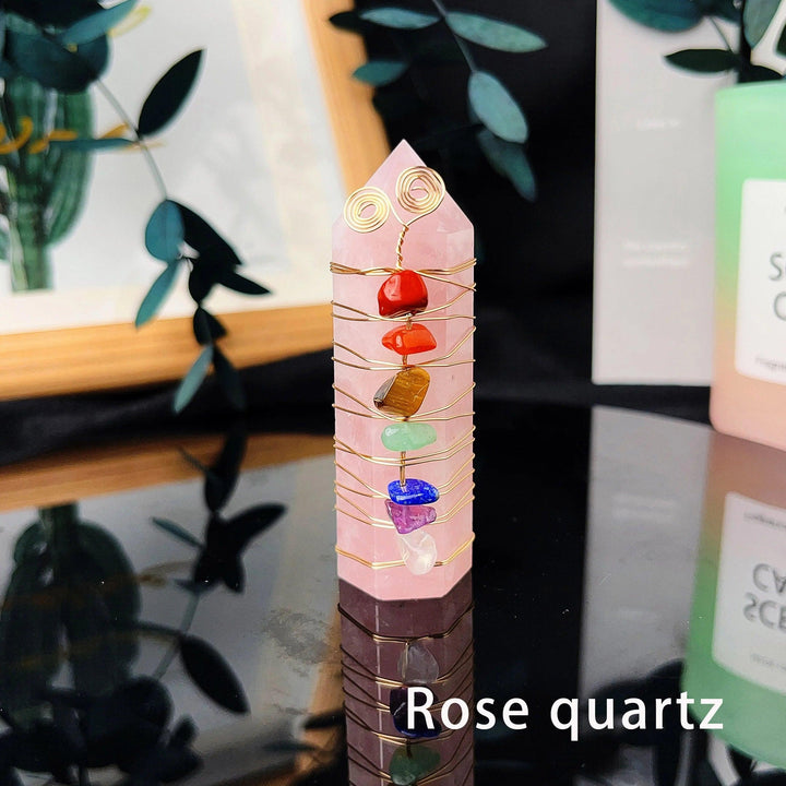Rose quartz crystal tower with seven chakra chips and gold copper wire winding, reflecting on a dark surface.