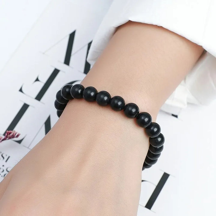 Shungite Bead Bracelet: black bead bracelet worn on a wrist against a white magazine page