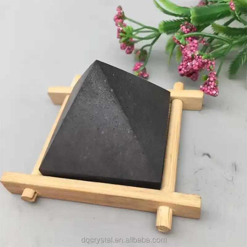 Satin black Shungite crystal pyramid on a wooden stand for Root chakra grounding, protection, and sacred energy work.