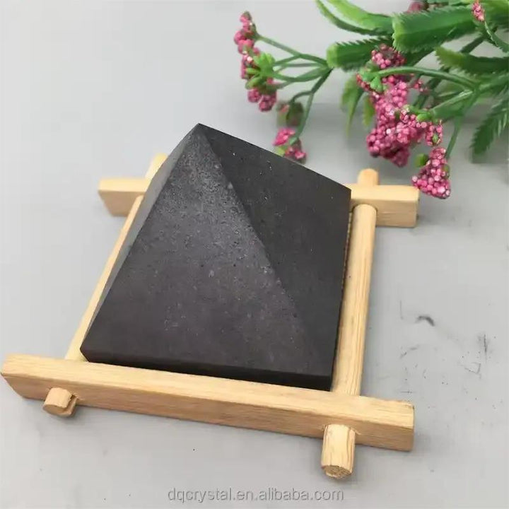 Satin black Shungite crystal pyramid on a wooden stand for Root chakra grounding, protection, and sacred energy work.