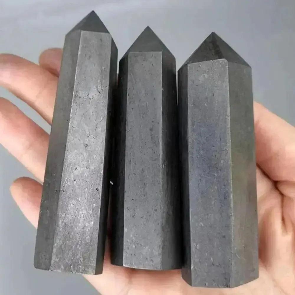 Three dark gray, hexagonal Shungite Crystal Towers held in a hand, offering EMF protection and grounding.