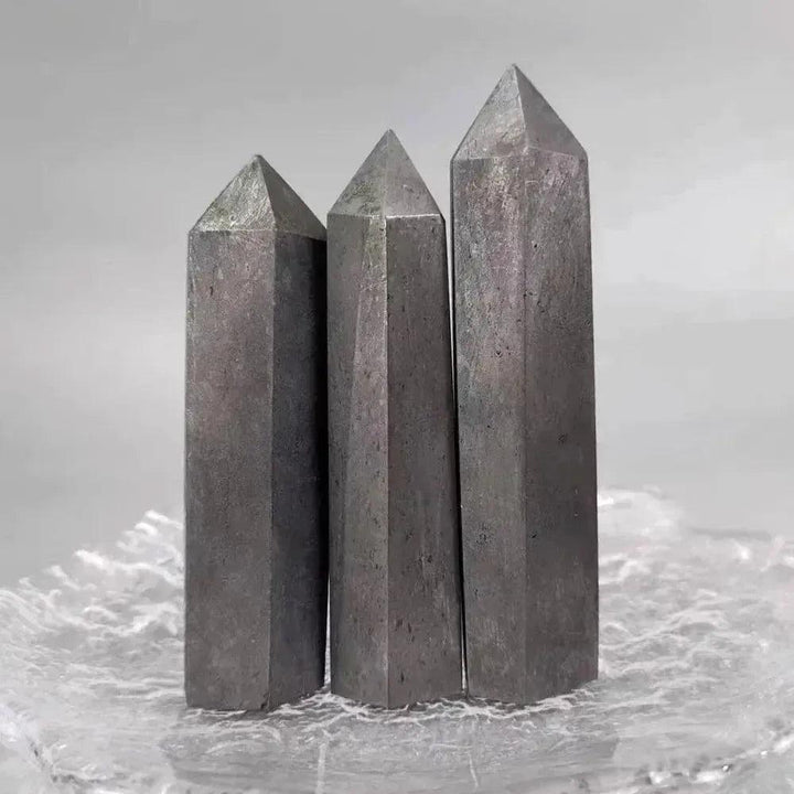 Three dark gray Shungite Crystal Towers from Crystal Destiny, with pointed tops, on a clear textured surface.