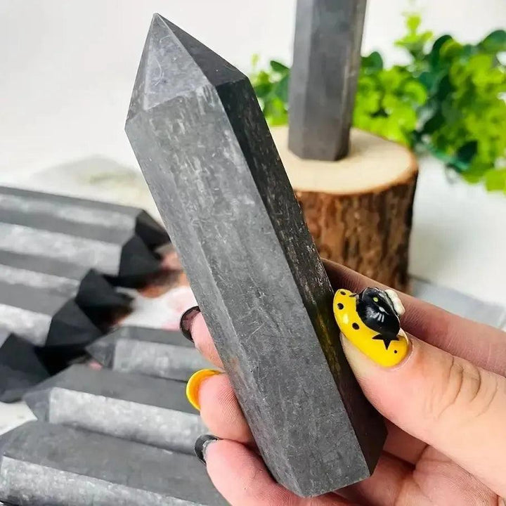 Dark gray Shungite Crystal Tower held by hand, offering EMF protection and grounding from Crystal Destiny.