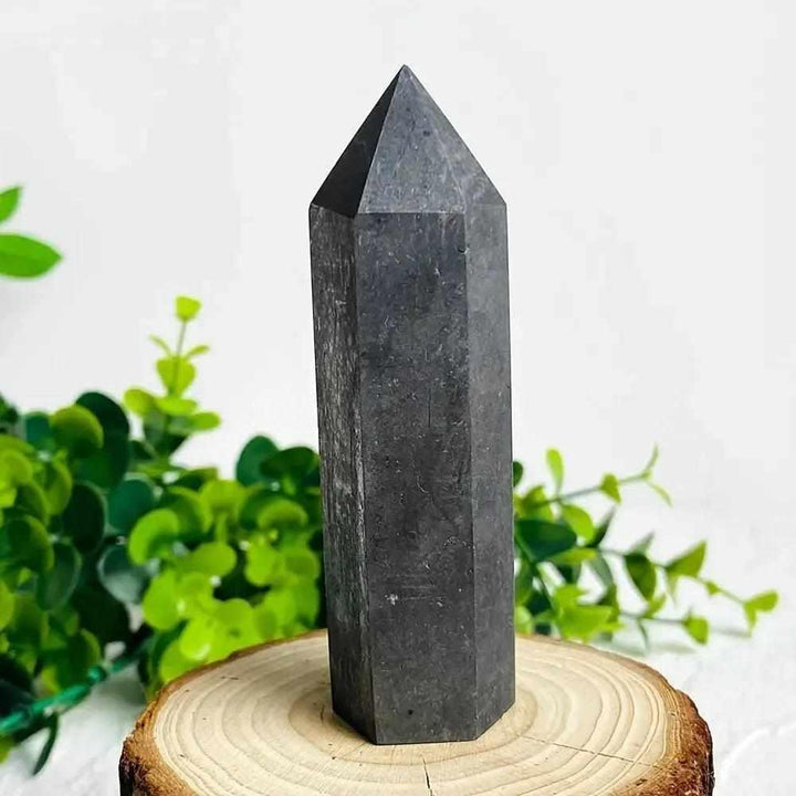 Deep matte black Shungite Crystal Tower, 90-110MM, for EMF protection and grounding, on a wood slice.