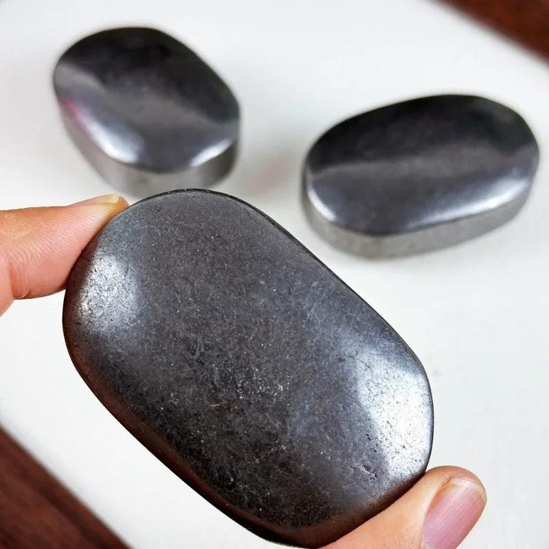 Smooth, polished black Shungite palm stone held in hand, perfect for grounding and protection against electronics.