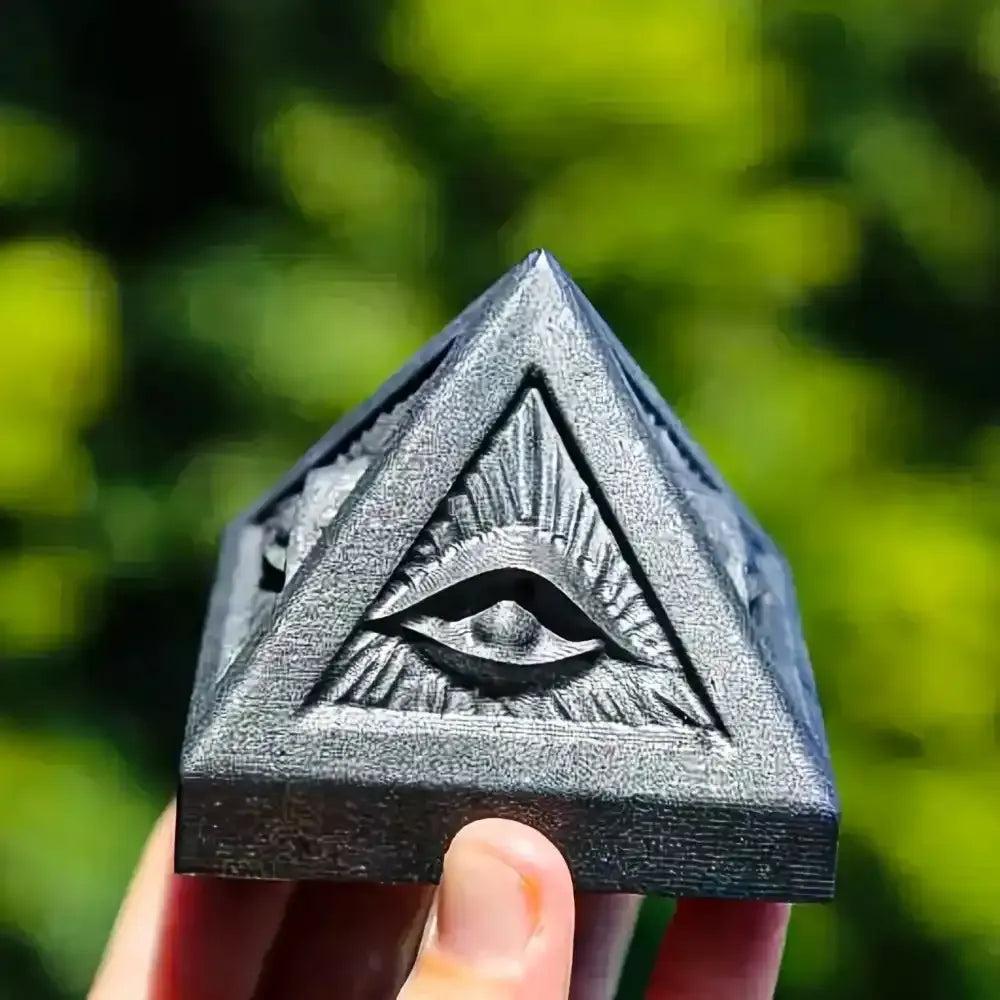 Hand-polished satin black Shungite pyramid featuring an engraved all-seeing eye for grounding and root chakra protection.