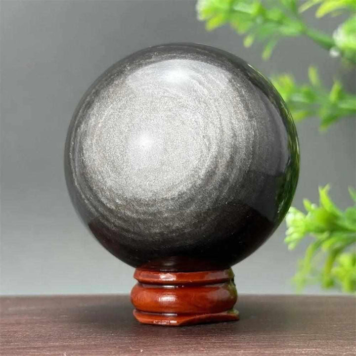 Polished Silver Sheen Obsidian sphere on a wooden base, featuring a glossy black surface with a radiant silvery shimmer.