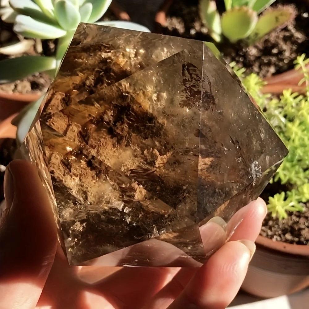 Polished smoky quartz crystal freeform, deep brown with translucent facets, held against a blurred succulent background.