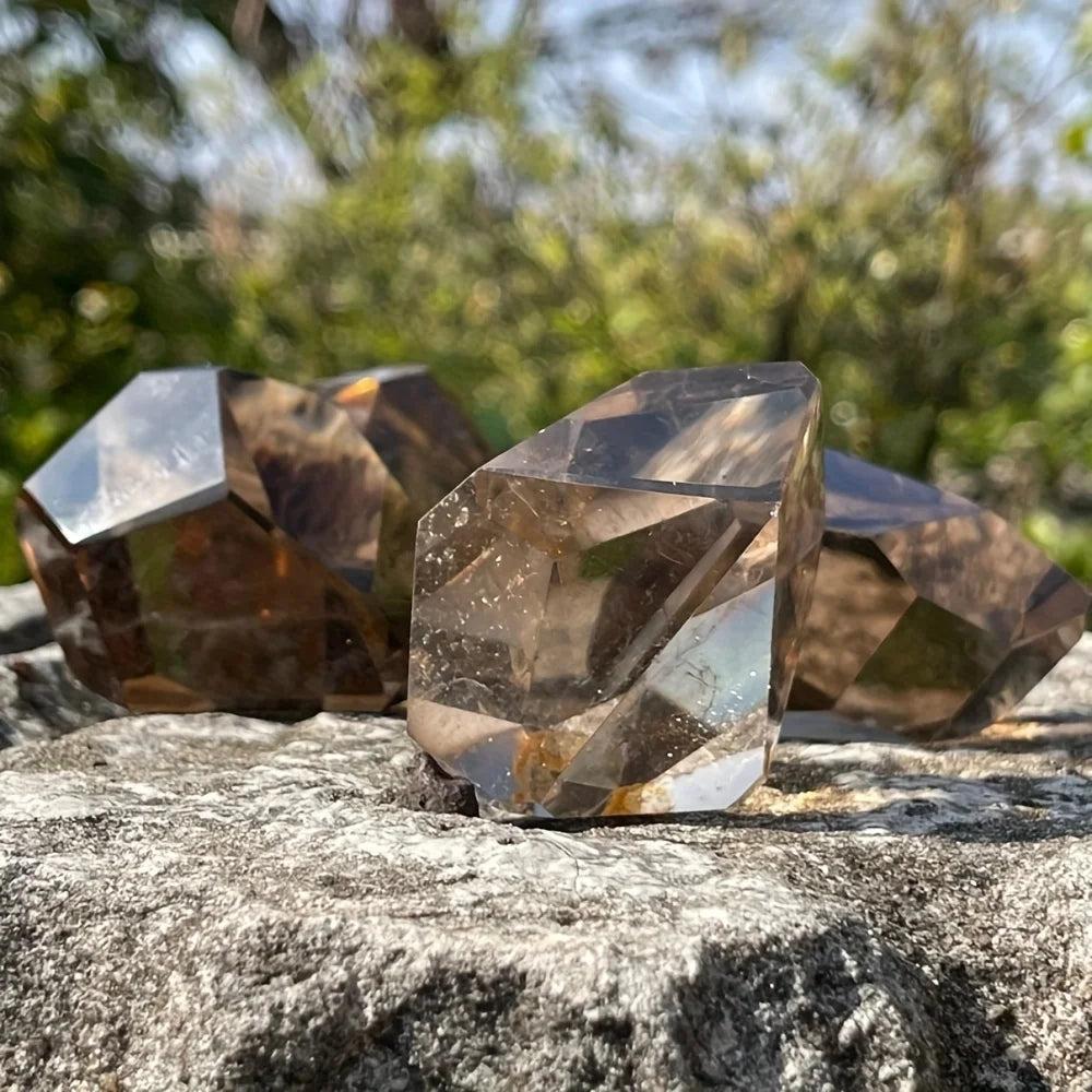 Polished, faceted Smoky Quartz crystal freeforms on a stone surface, showcasing their grounding, translucent brown-black hues.