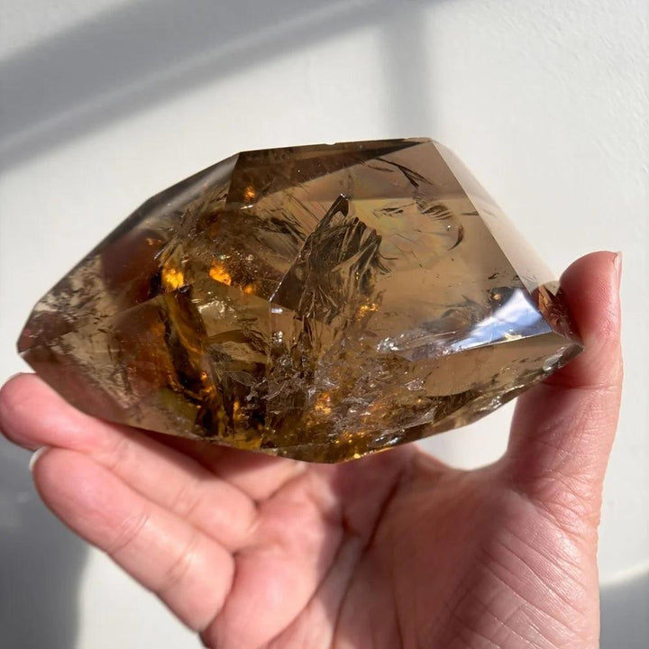 Polished, translucent brown Smoky Quartz crystal freeform held in a hand, showcasing its grounding energy.