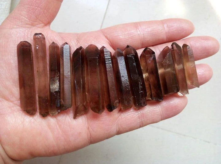 Hand holding a bulk lot of natural Smoky Quartz crystal points, showcasing their deep, grounding brown hues.