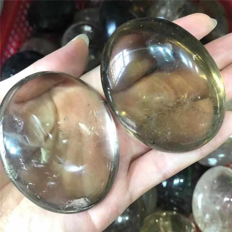 Two smooth, translucent smoky quartz palm stones with grounding brown and gray tones held in a hand for meditation.