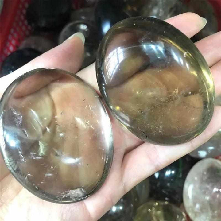 Two smooth, translucent smoky quartz palm stones with grounding brown and gray tones held in a hand for meditation.