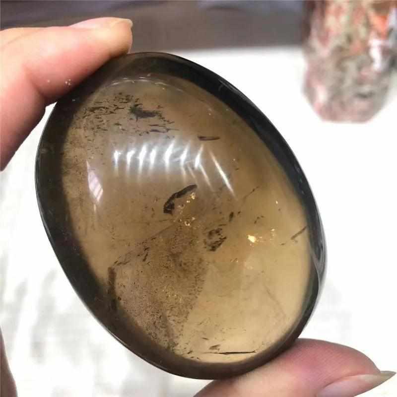 Smooth, translucent smoky quartz palm stone with grounding brown tones, perfect for meditation and stress relief.