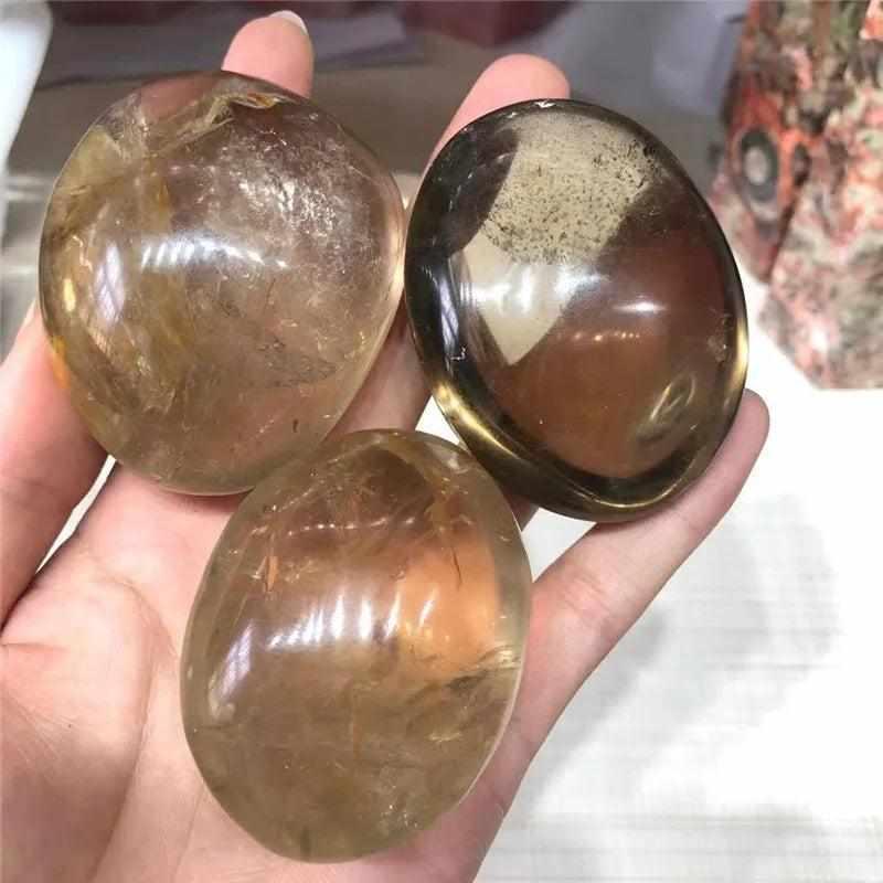 Three smooth, translucent smoky quartz palm stones in brown and gray, perfect for grounding and meditation.