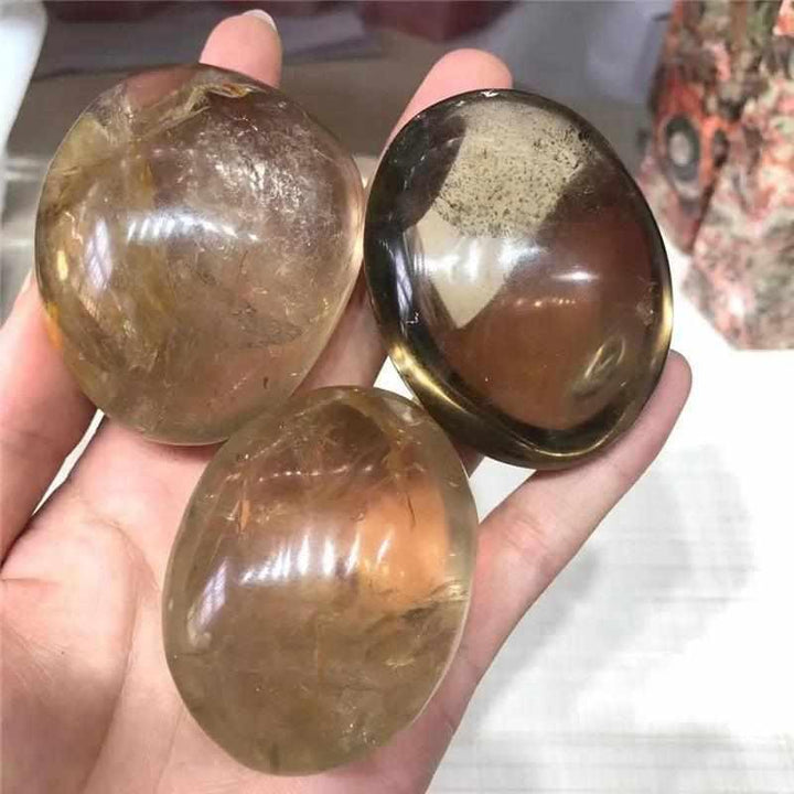 Three smooth, translucent smoky quartz palm stones in brown and gray, perfect for grounding and meditation.