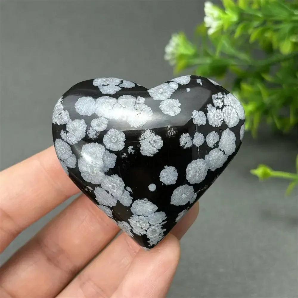 Polished Snowflake Obsidian crystal heart, black with white snowflake patterns, held in a hand.