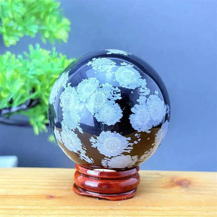 Snowflake Obsidian Sphere: Polished black volcanic crystal with striking white snowflake patterns on a wooden stand.