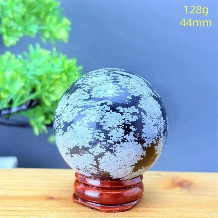 Snowflake Obsidian Sphere: Deep black volcanic crystal with striking white snowflake patterns, 128g, 44mm, on a wooden stand.