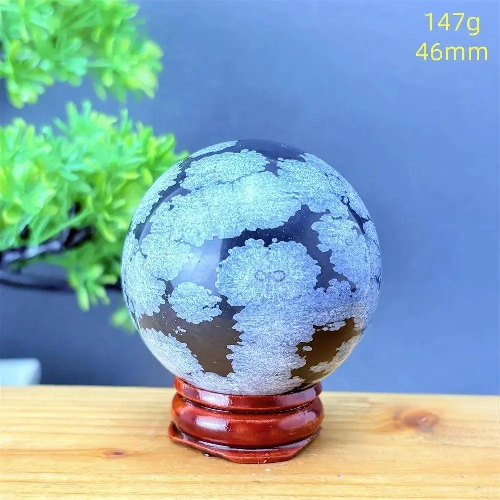 Snowflake Obsidian Sphere: Polished black volcanic crystal with striking white snowflake patterns on a wooden stand.