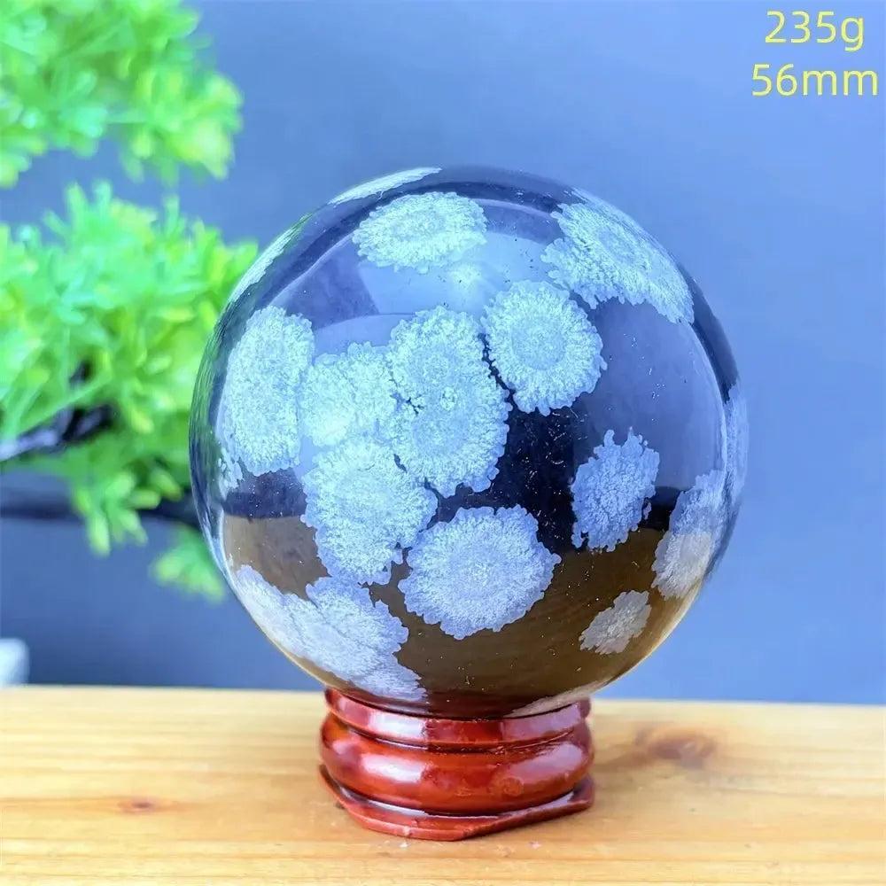 Snowflake Obsidian Sphere: Polished black volcanic crystal with striking white snowflake patterns on a wooden stand.