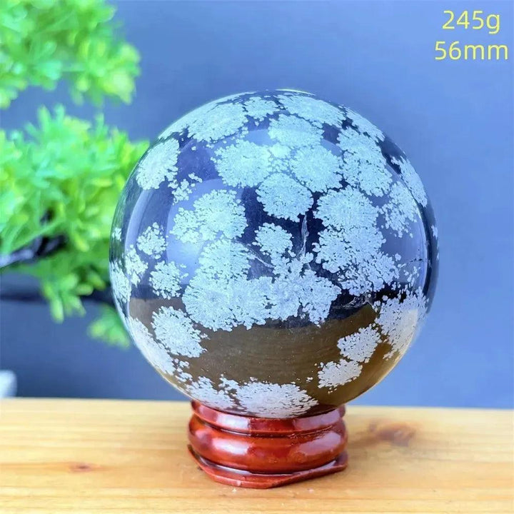 Snowflake Obsidian Sphere: Polished black volcanic crystal with striking white snowflake patterns on a wooden stand.