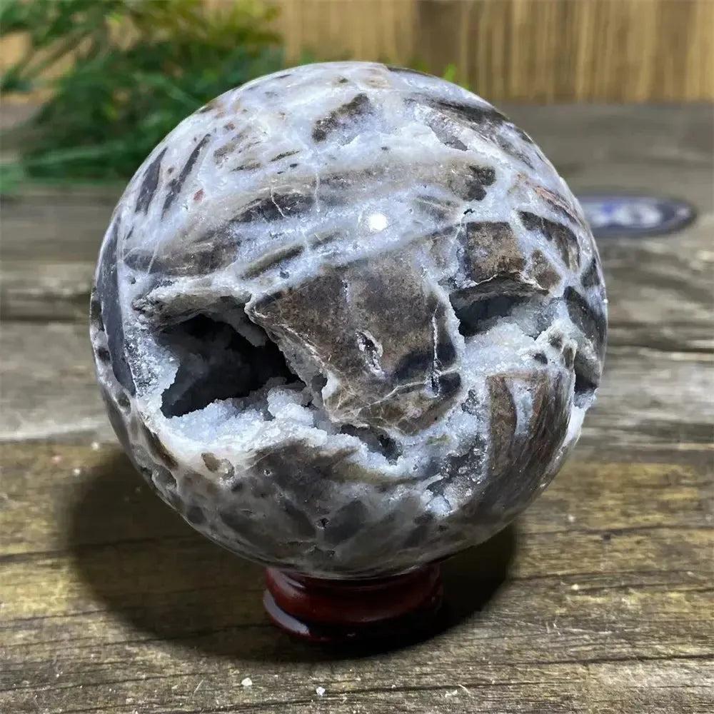 Polished Sphalerite sphere with metallic luster, rich amber tones, and a geode opening on a red stand.