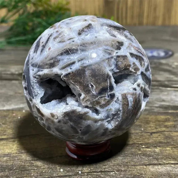 Polished Sphalerite sphere with metallic luster, rich amber tones, and a geode opening on a red stand.