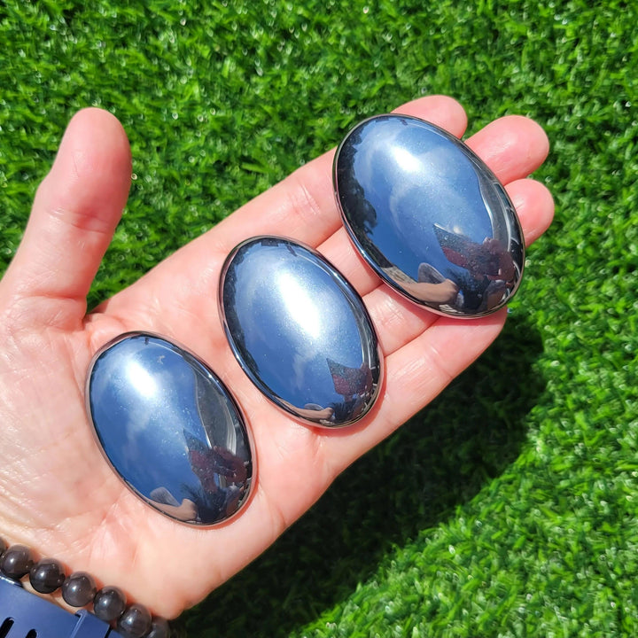 Three metallic Terahertz Crystal Palm Stones held in a hand for grounding and vitality.