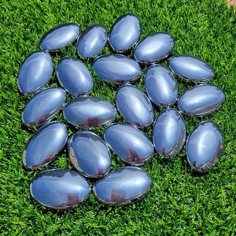 Polished Terahertz Crystal Palm Stones with a metallic silver-gray finish on green grass for grounding energy.