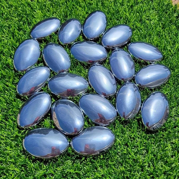 Polished Terahertz Crystal Palm Stones with a metallic silver-gray finish on green grass for grounding energy.
