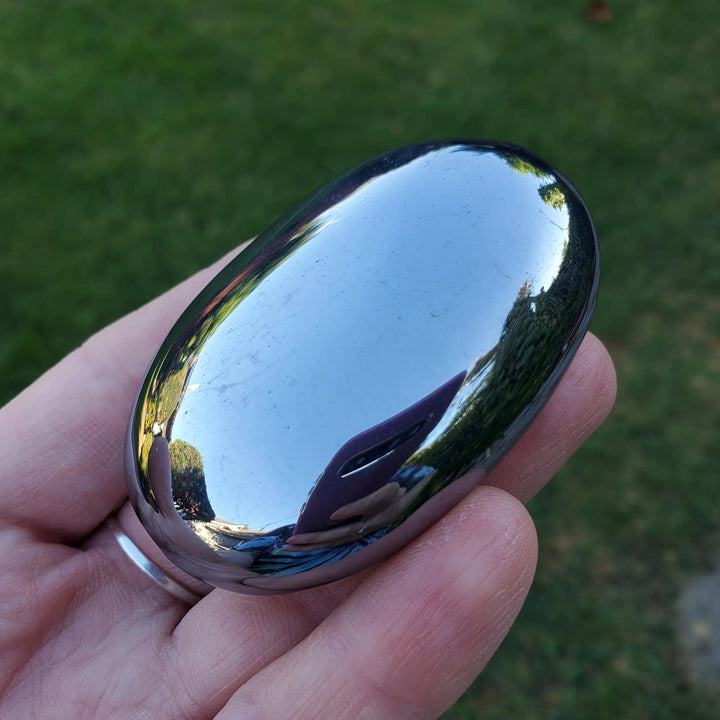 Polished Terahertz Crystal Palm Stone with a reflective, metallic silver-gray finish for grounding energy.