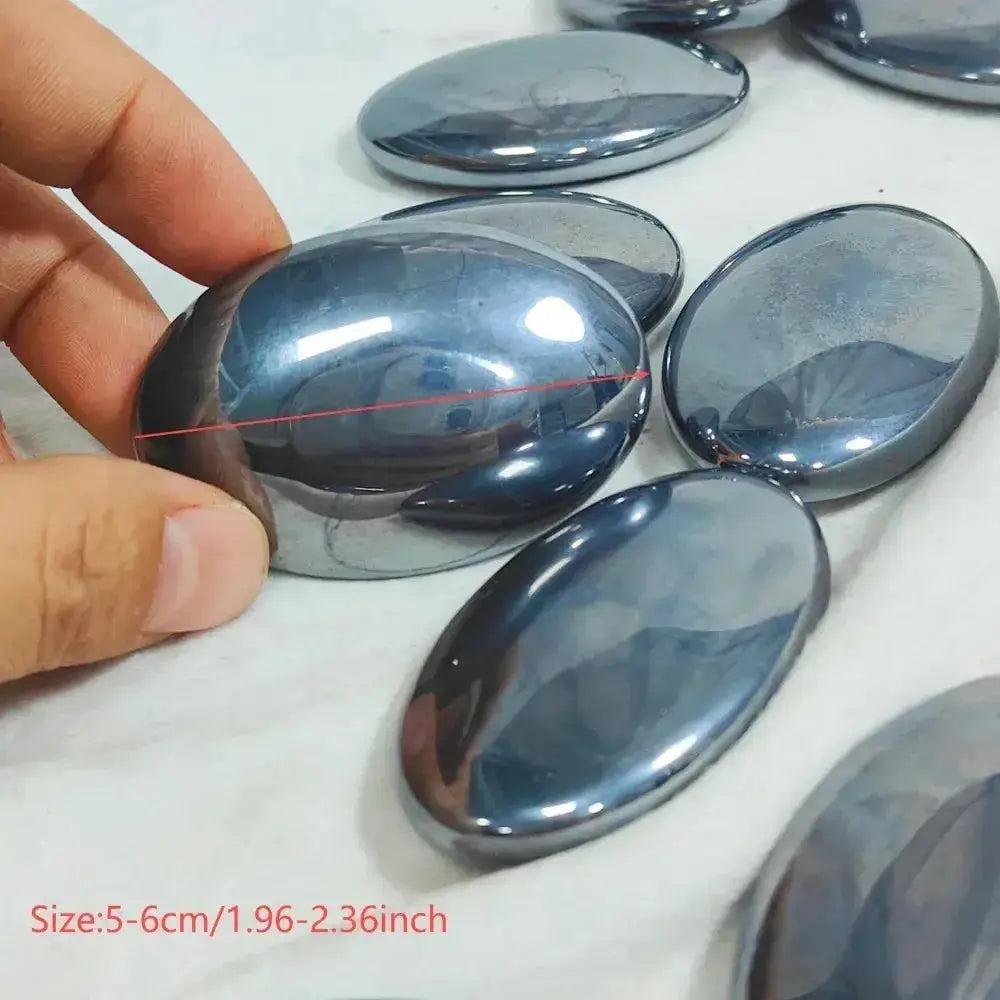Hand holding a polished, dark metallic Terahertz crystal palm stone, oval and smooth, for focus and clarity.
