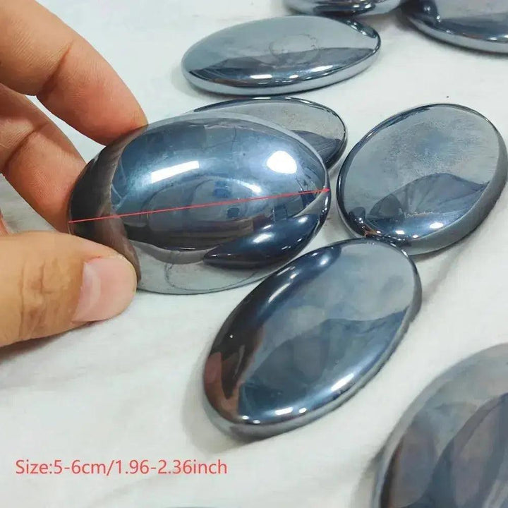 Hand holding a polished, dark metallic Terahertz crystal palm stone, oval and smooth, for focus and clarity.