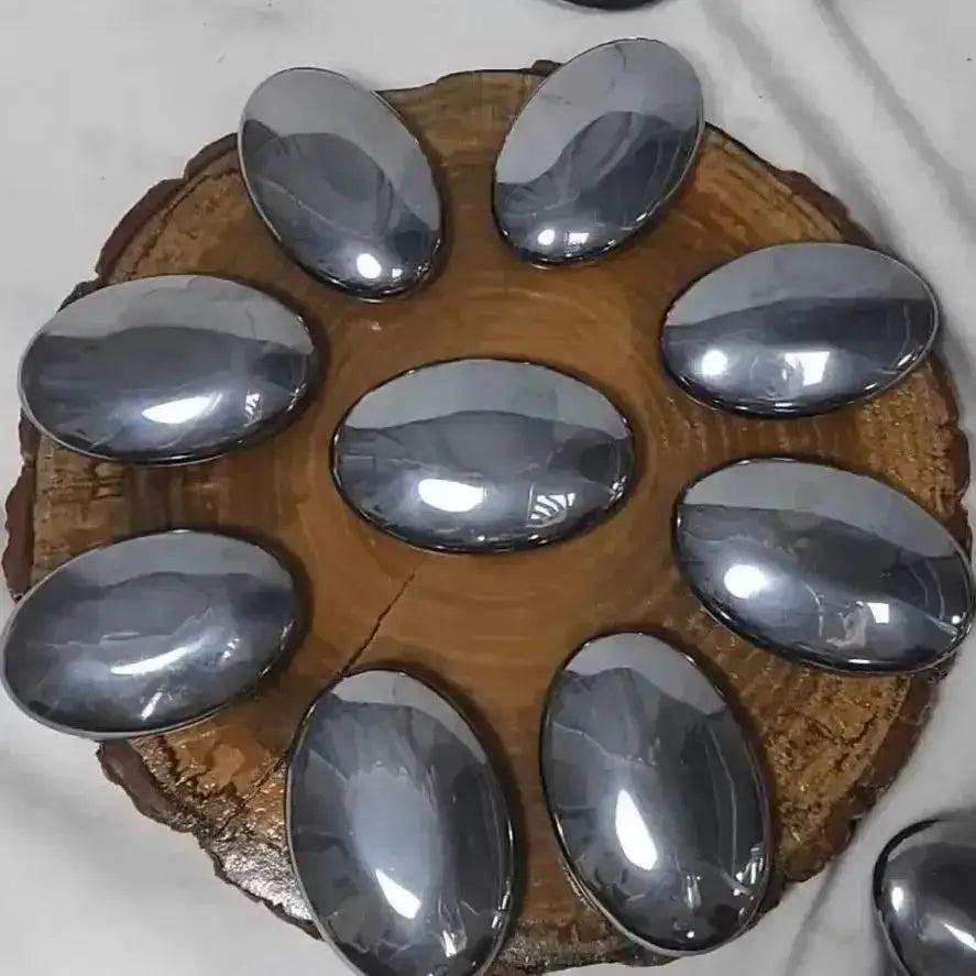 Polished Terahertz crystal palm stones, smooth and metallic gray, arranged on a rustic wooden slice.