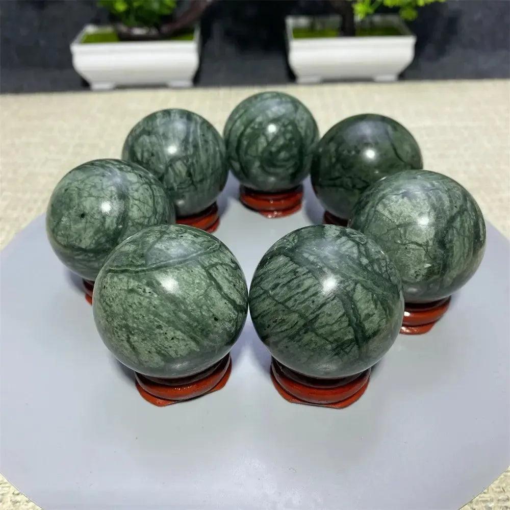 Seven polished Tibetan Jade crystal spheres, rich earthy green with natural variations, on wooden stands from Crystal Destiny.