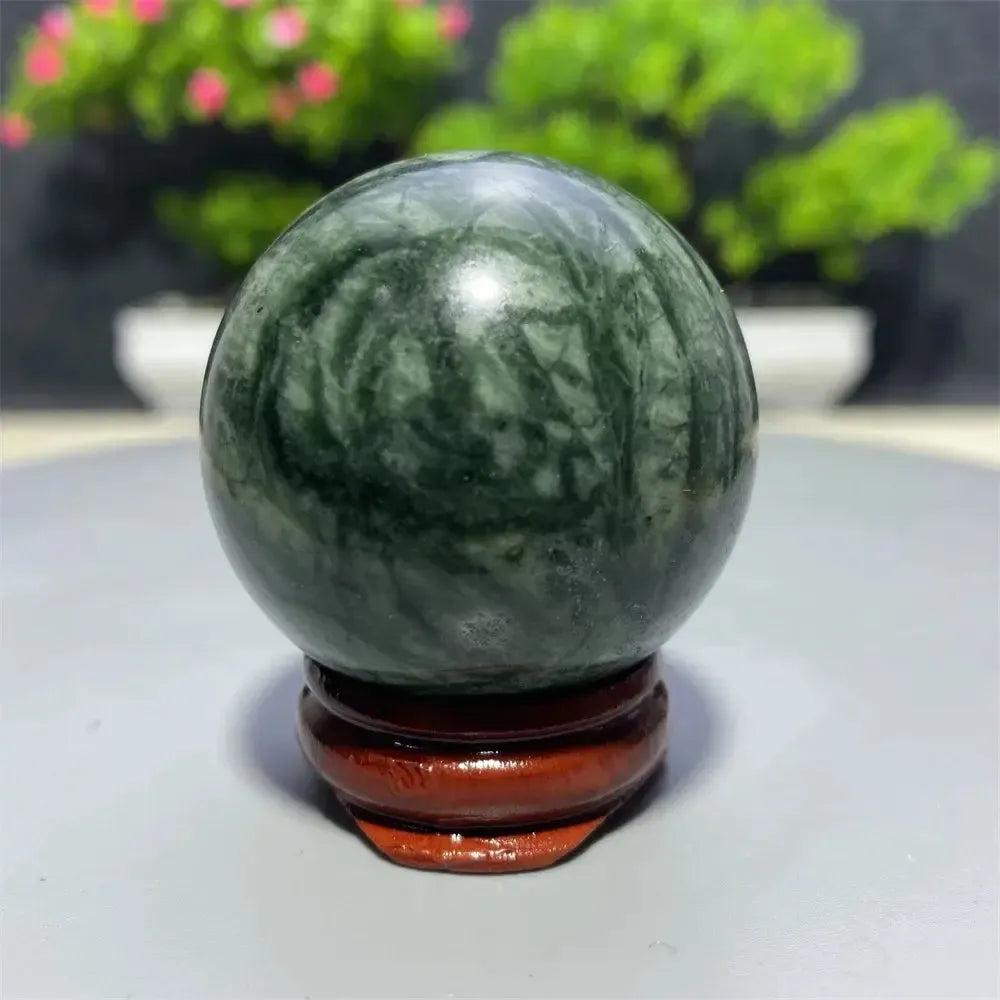 Polished dark green Tibetan Jade Crystal Sphere with natural swirling patterns on a wooden stand from Crystal Destiny.