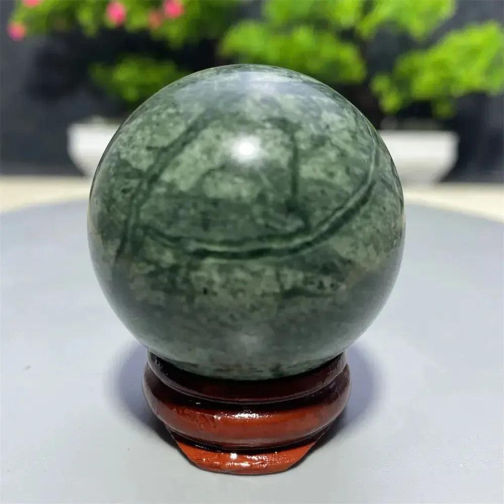 Smooth, polished Tibetan Jade Crystal Sphere in earthy green with natural patterns, on a wooden stand from Crystal Destiny.
