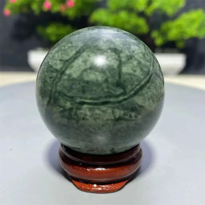 Smooth, polished Tibetan Jade Crystal Sphere in earthy green with natural patterns, on a wooden stand from Crystal Destiny.