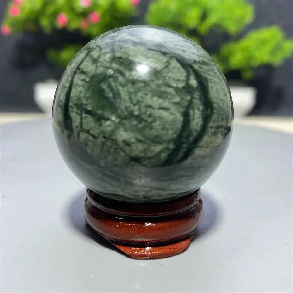 Polished dark green Tibetan Jade Crystal Sphere with natural black veining on a wooden stand from Crystal Destiny.