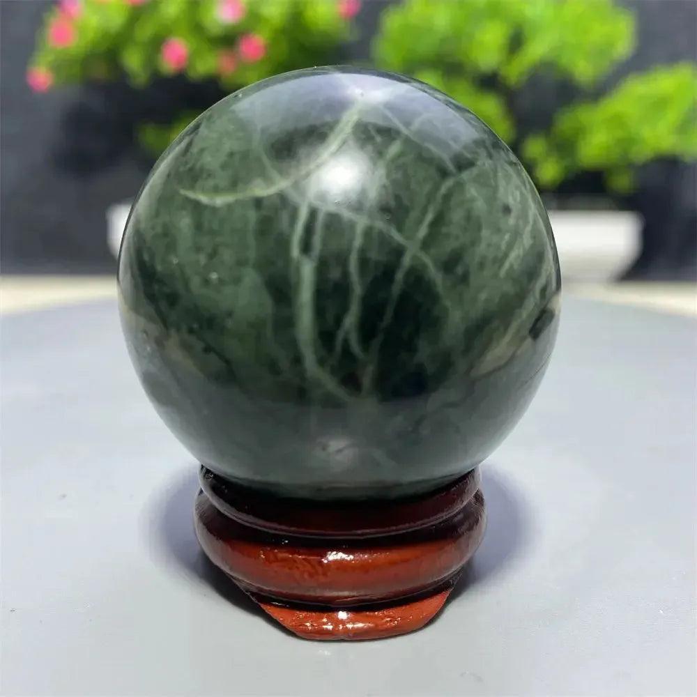 Polished dark green Tibetan Jade Crystal Sphere with natural white veins on a wooden stand from Crystal Destiny.