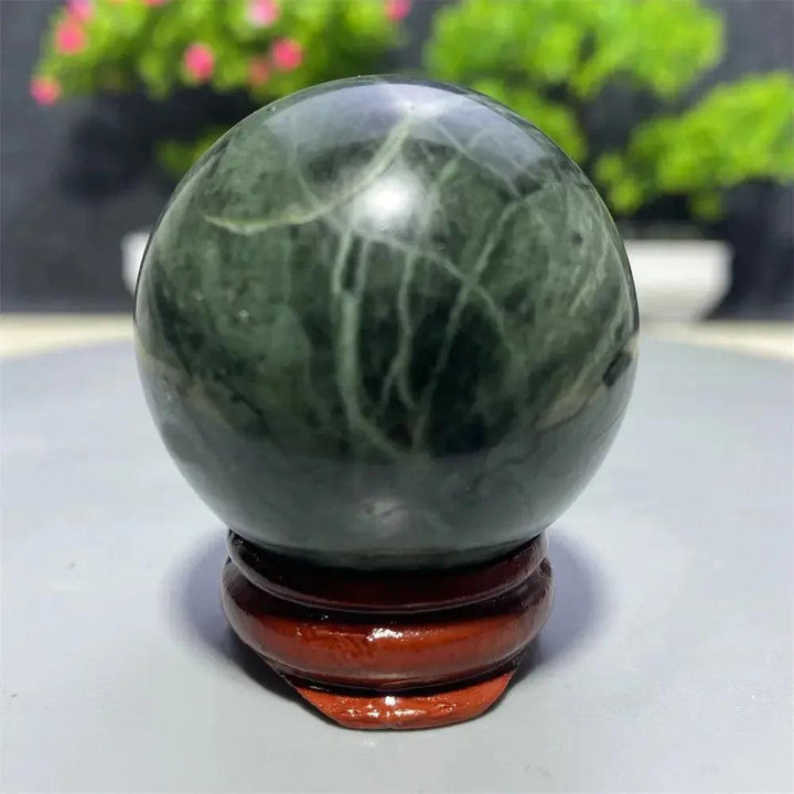 Polished dark green Tibetan Jade Crystal Sphere with natural white veins on a wooden stand from Crystal Destiny.