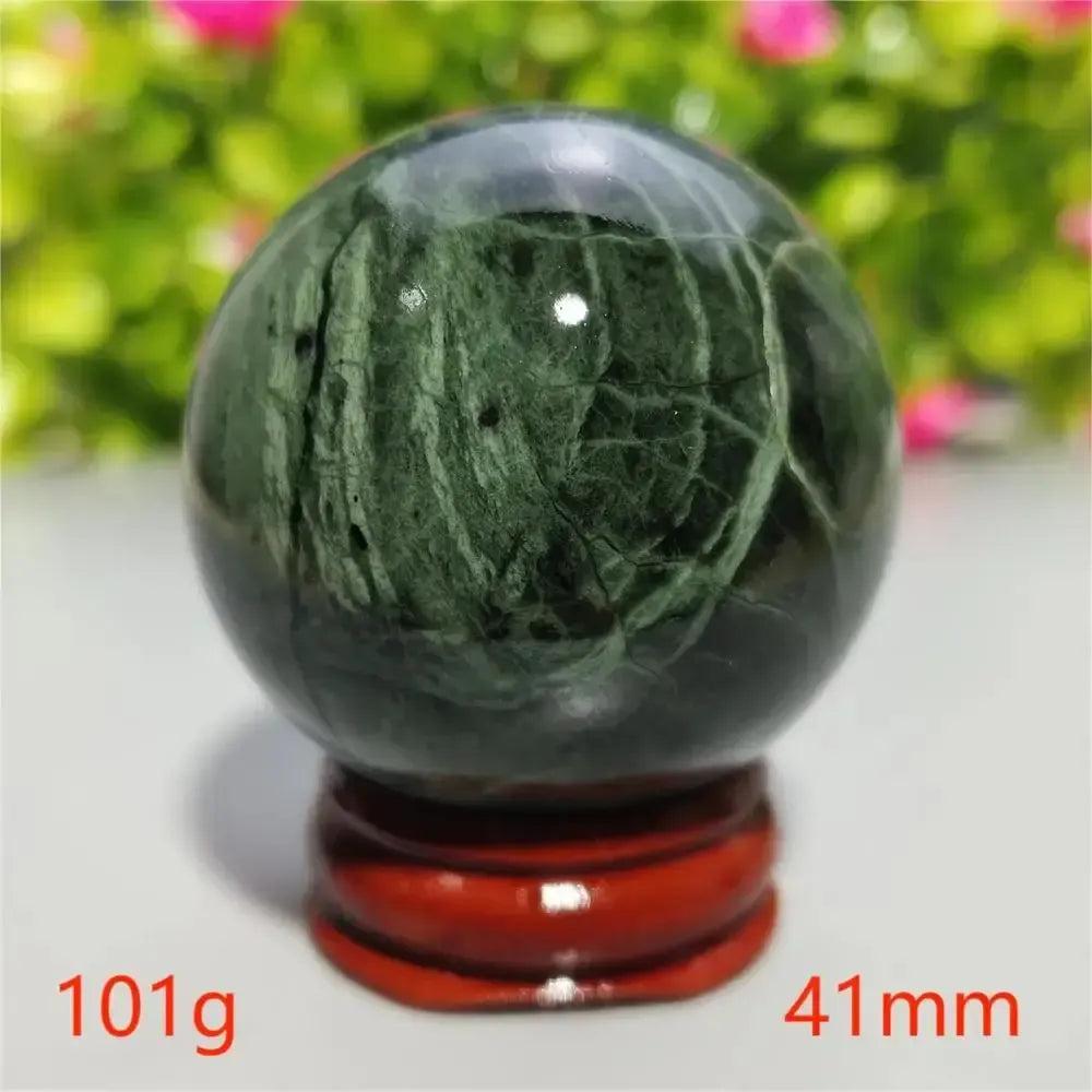 Smooth, dark green Tibetan Jade Crystal Sphere with natural patterns on a red wooden stand from Crystal Destiny.
