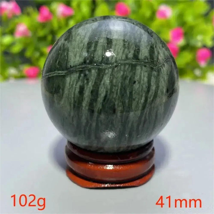 Polished dark green Tibetan Jade Crystal Sphere from Crystal Destiny, displaying natural stripes on a wooden stand.