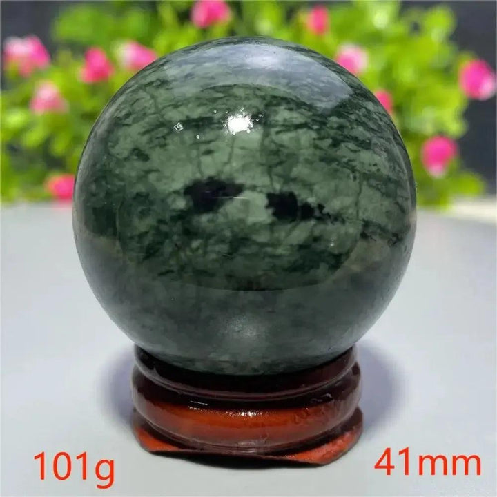 Polished dark green Tibetan Jade Crystal Sphere with natural black inclusions on a wooden stand from Crystal Destiny.