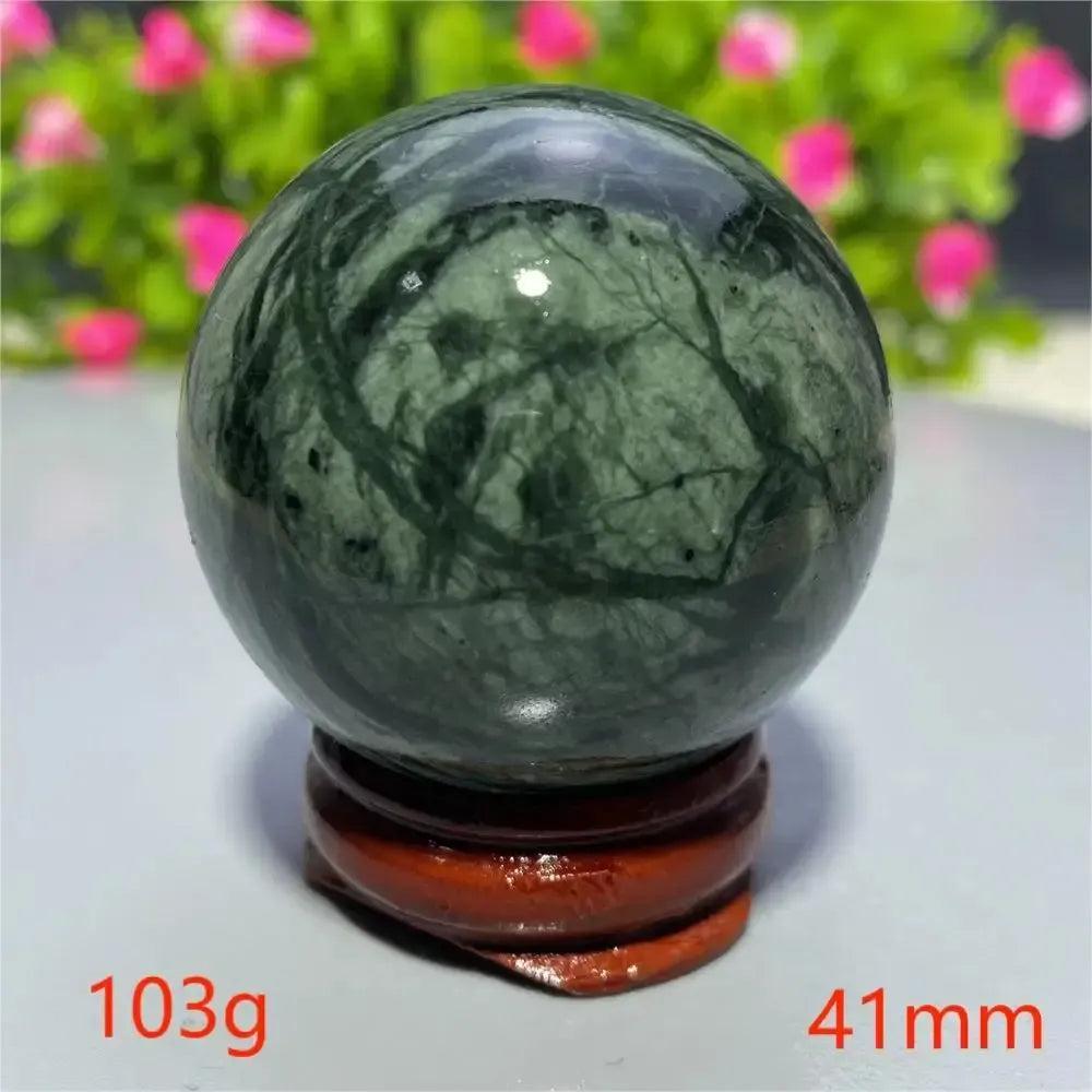 Polished dark green Tibetan Jade crystal sphere with natural black veining, displayed on a wooden stand. Crystal Destiny.