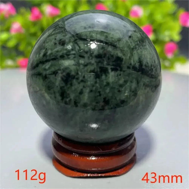 Polished dark green Tibetan Jade crystal sphere on a wooden stand from Crystal Destiny, promoting calm and balance.