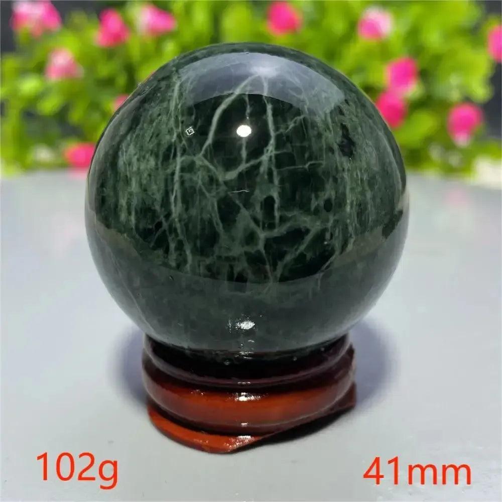 Polished dark green Tibetan Jade Crystal Sphere with white veins on a wooden stand from Crystal Destiny.