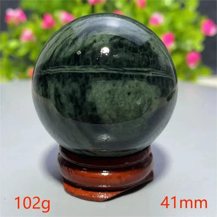 Polished dark green Tibetan Jade Crystal Sphere on a wooden stand from Crystal Destiny, promoting vitality and peace.